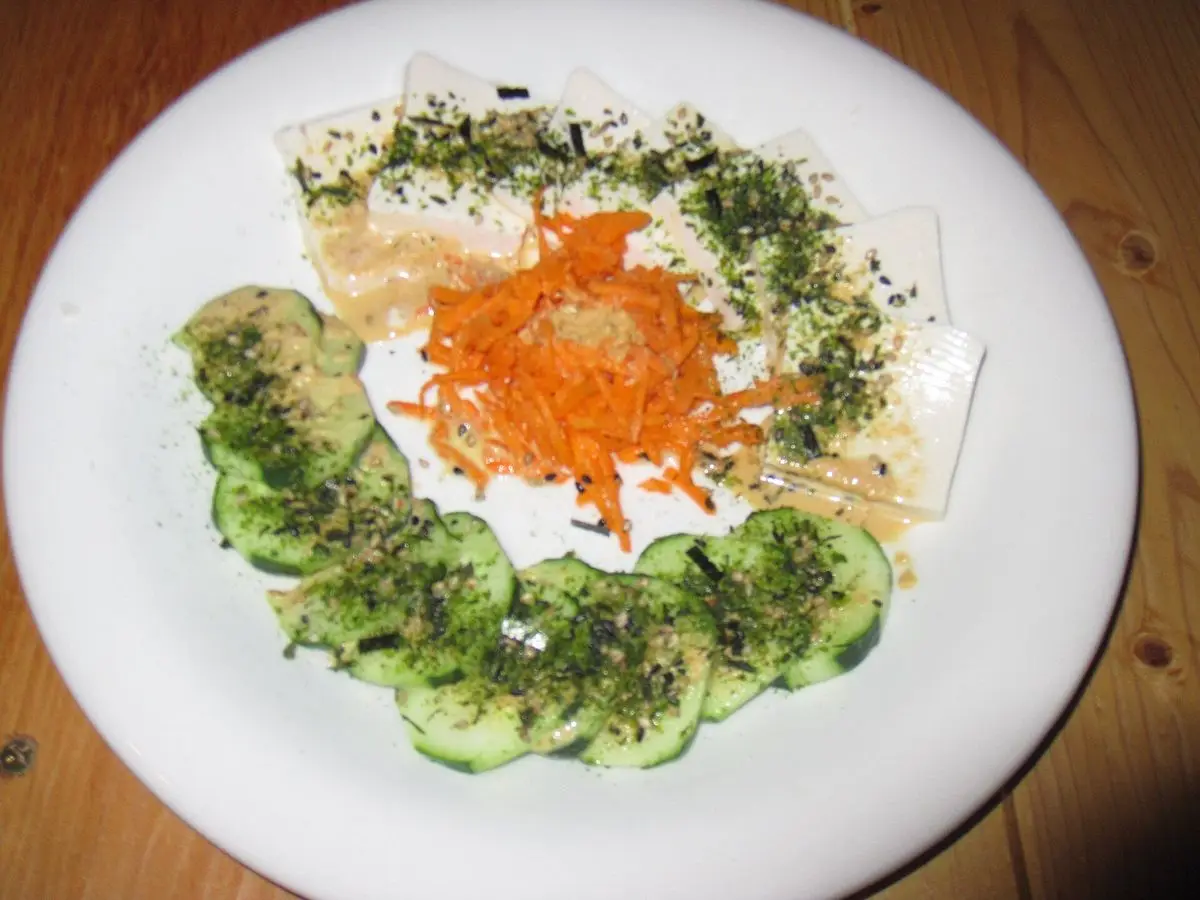 Plato blanco con dados de tofu blanco sobre rodajas de pepino, zanahoria rallada y algas por encima