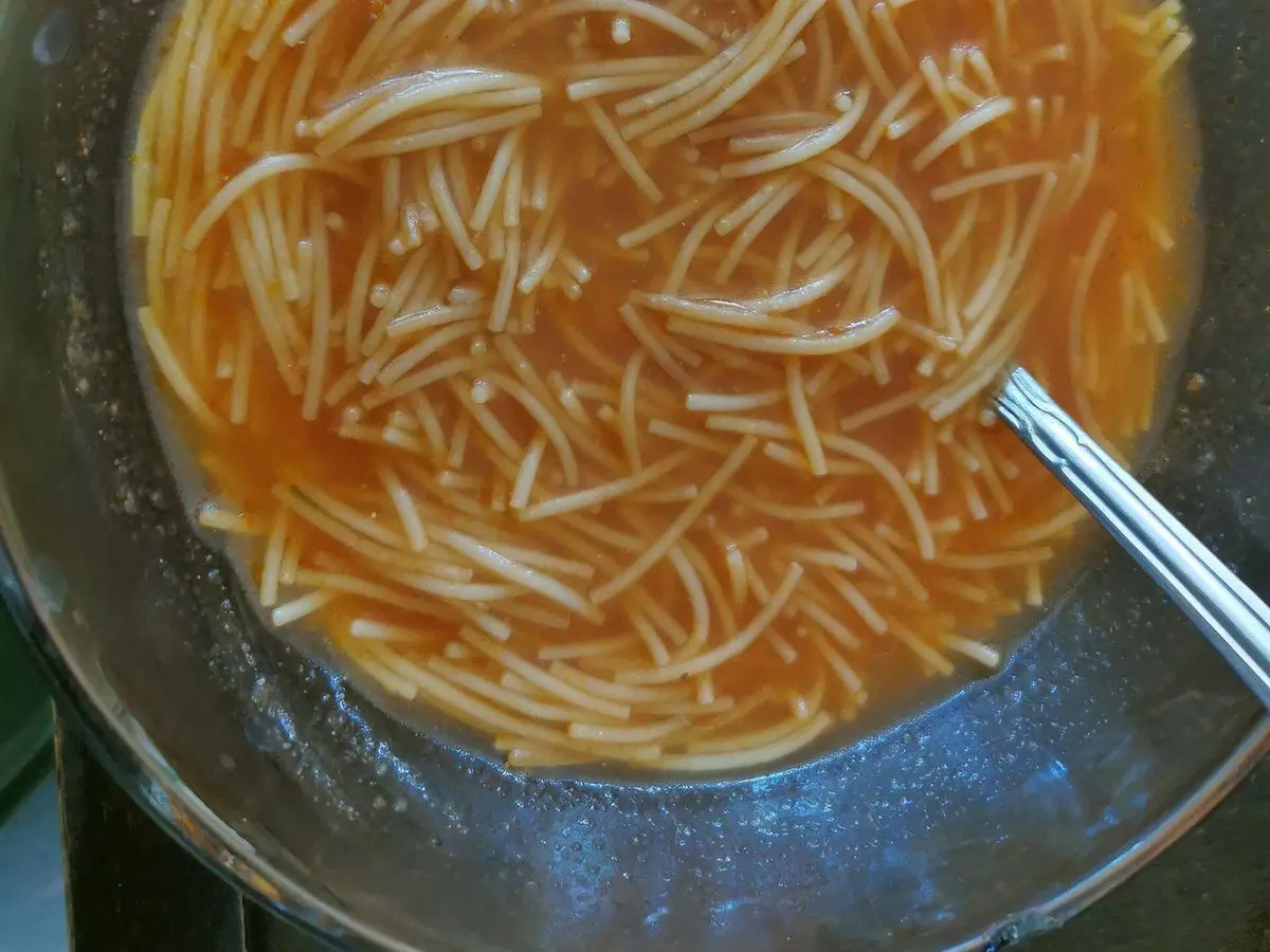Plato hondo de fideos finos en caldo de tomate anaranjado con una cuchara