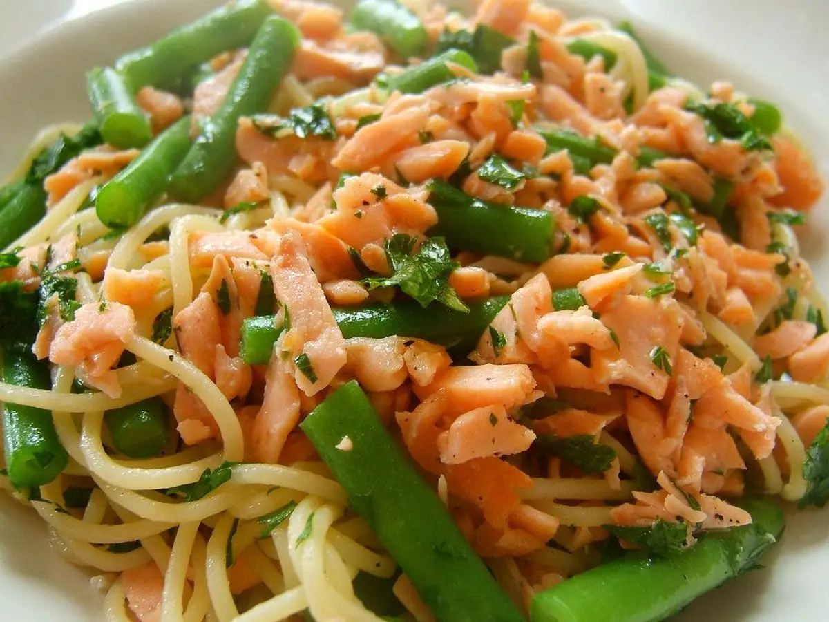 Fideos con salmón desmenuzado, judías verdes y zanahoria en un plato blanco
