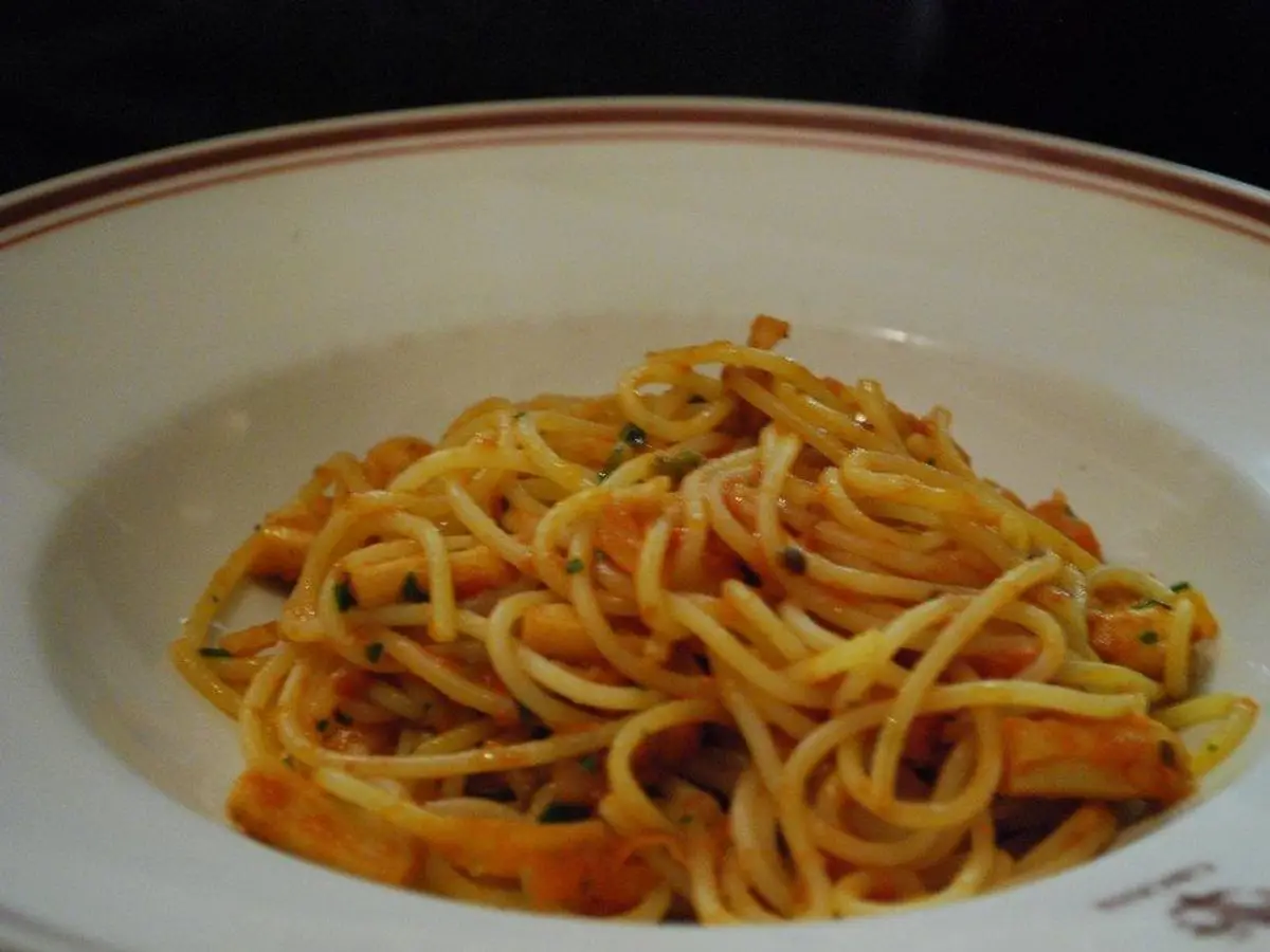Plato hondo de espaguetis con trozos de calamar en salsa de tomate y perejil picado