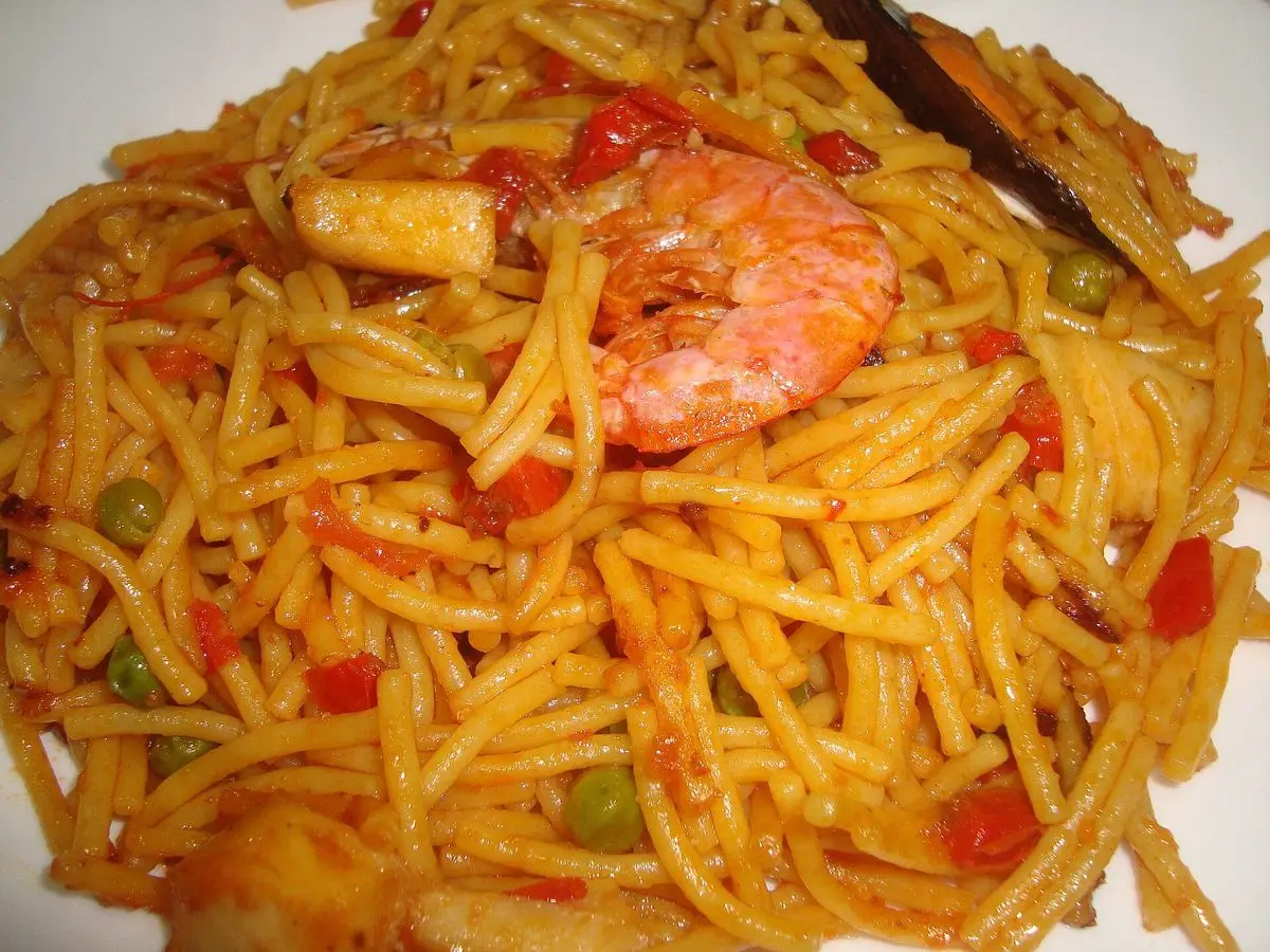 Plato de fideuá dorada con pimiento rojo, guisantes y una gamba entera
