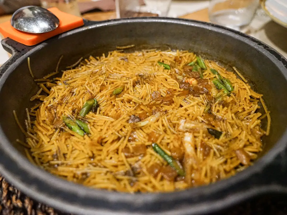 Fideuá de fideo fino dorado con judías verdes y tropezones en una cazuela negra