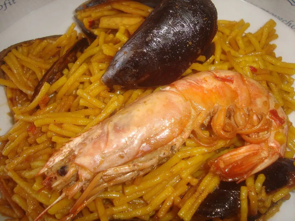 Fideuá dorada con una gamba grande y mejillones sobre un plato blanco