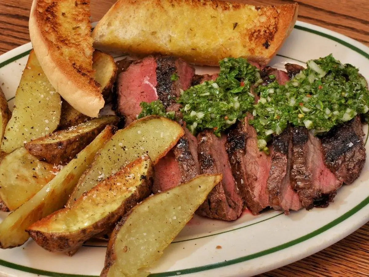Filetes de ternera laminados con chimichurri junto a gajos de patata asada y pan tostado