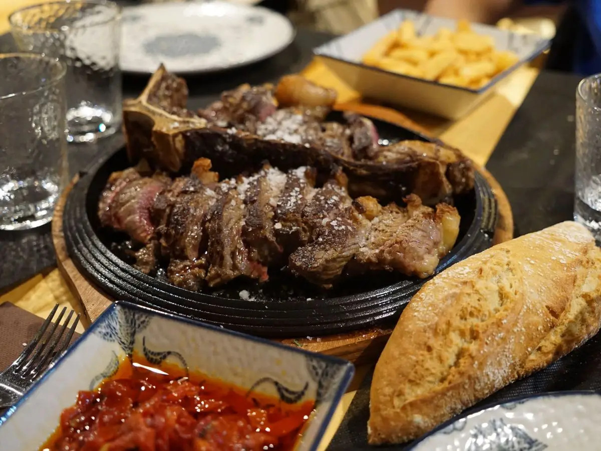 Filete de ternera a la parrilla en rodajas sobre una plancha de hierro, con pan, patatas fritas y salsa roja