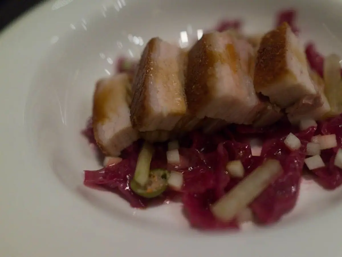 Tacos de panceta de cerdo sobre lombarda braseada con manzana en dados en un plato blanco