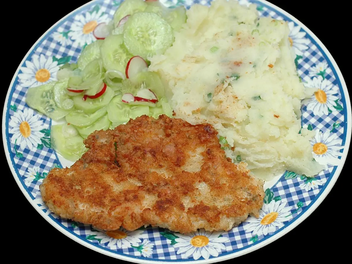 Filete de pavo empanado con puré de patata y ensalada de pepino y rábano en un plato de cuadros