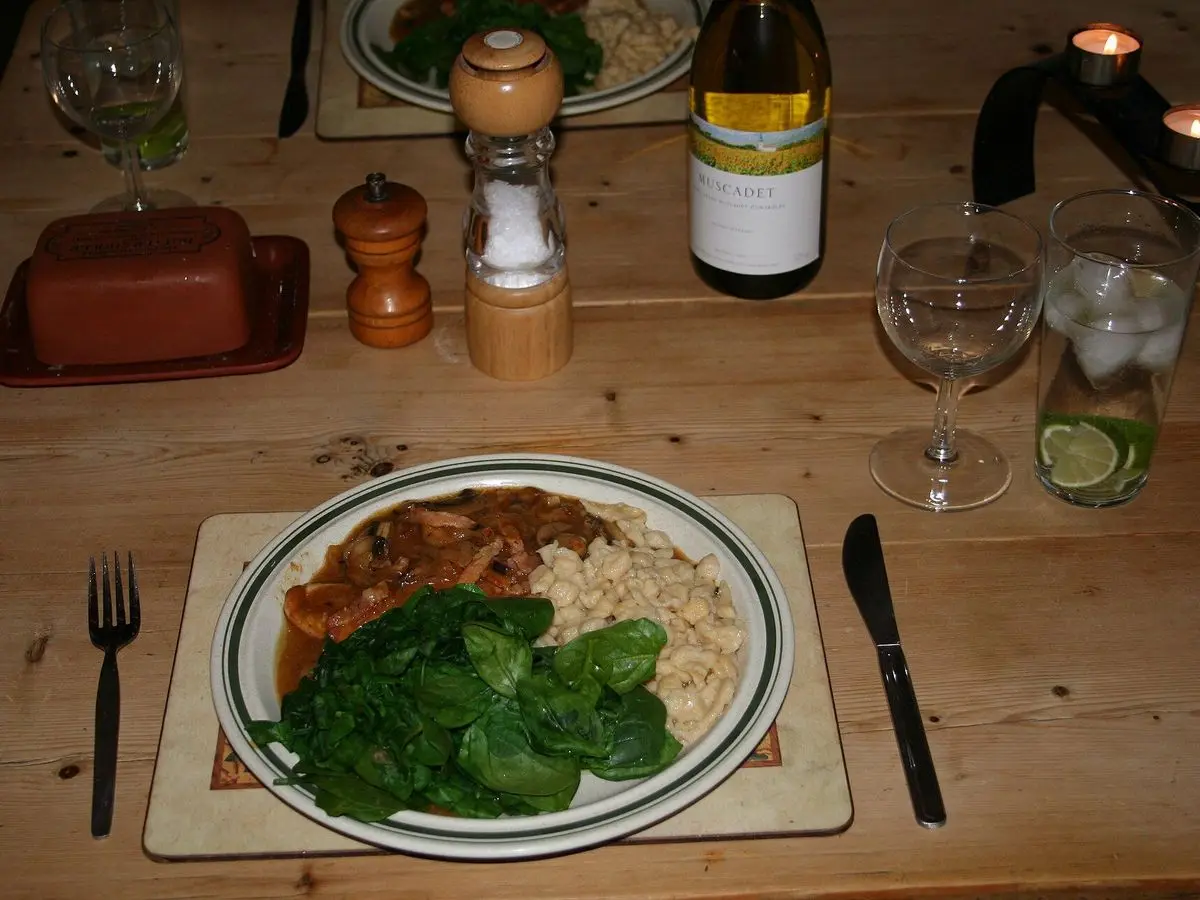 Plato con escalopes de pavo en salsa de champiñones, espinacas salteadas y guarnición sobre una mesa de madera