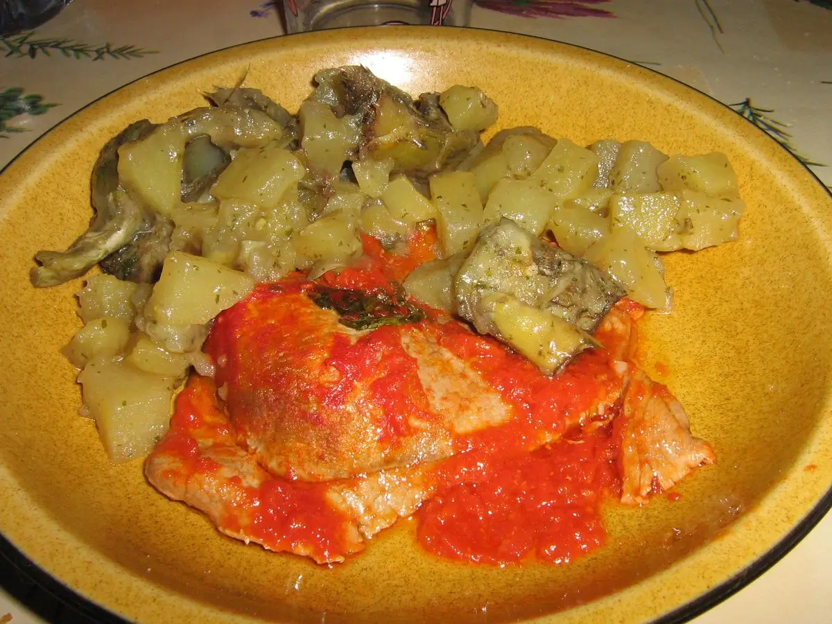 Plato amarillo con filete de ternera en salsa de tomate acompañado de patatas y alcachofas