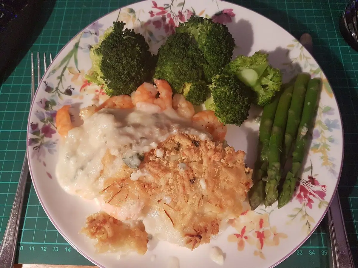 Fish pie con gambas, brócoli y espárragos verdes en un plato de flores