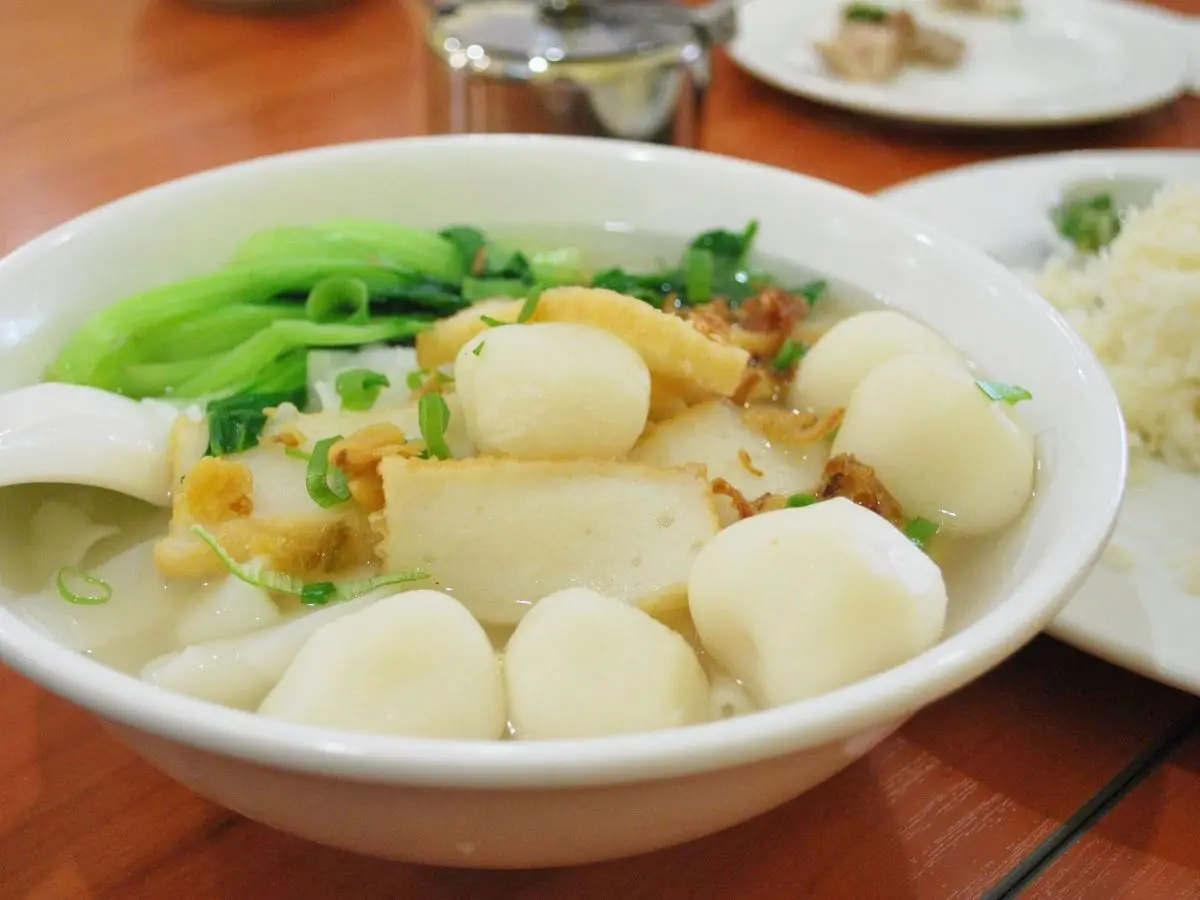 Cuenco de albóndigas de pescado blancas en caldo claro con hojas verdes y cuchara