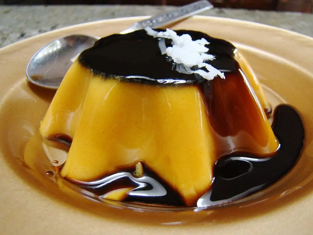 Flan dorado desmoldado con caramelo oscuro y coco rallado por encima en un plato