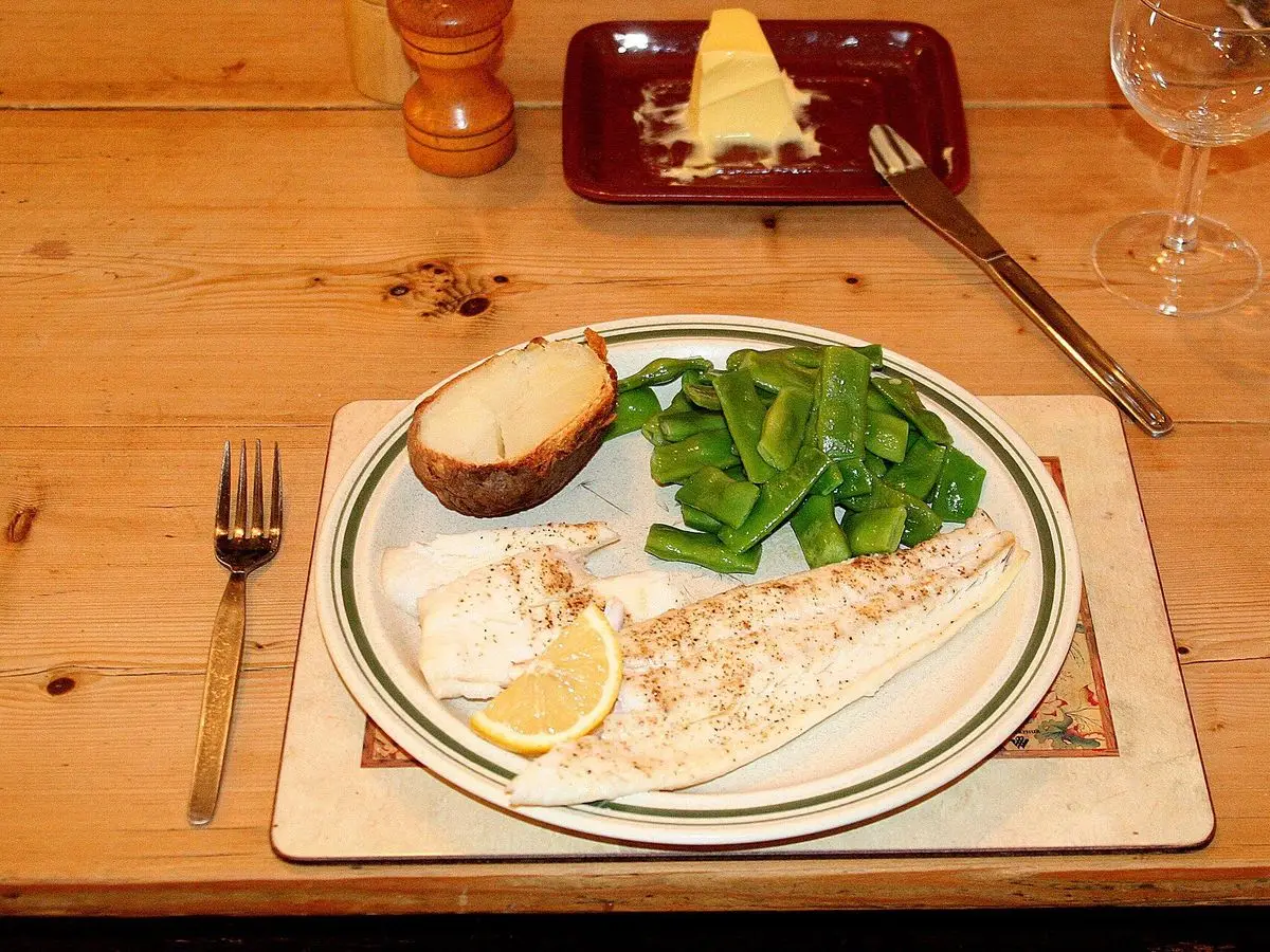 Filete de fletán cocinado con una rodaja de limón y judías verdes en un plato sobre mesa de madera