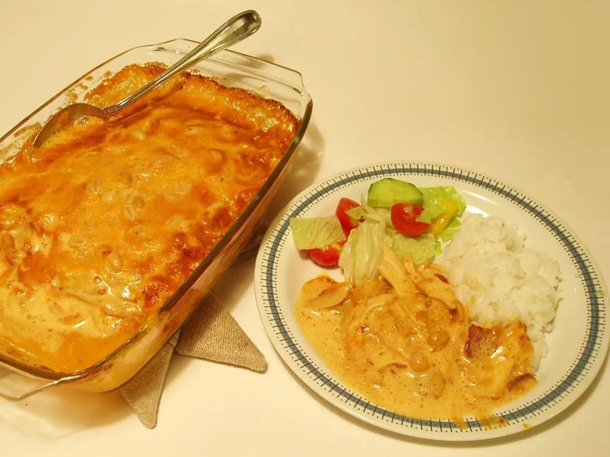 Fuente de cristal con pollo gratinado en salsa y un plato con arroz, ensalada y ración servida
