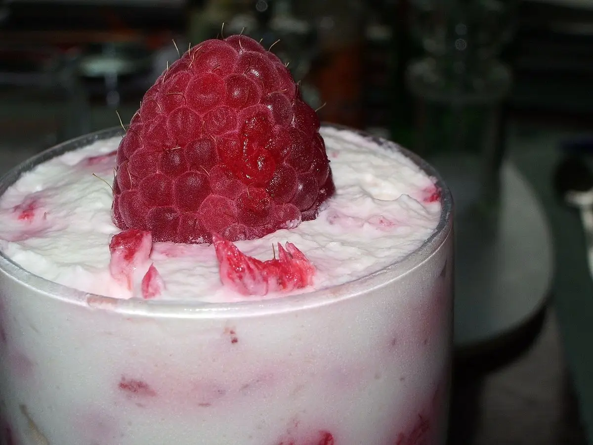 Vaso de crema blanca batida veteada de fruta roja y coronada con una frambuesa