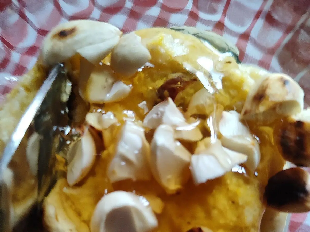 Postre cremoso amarillo de millo con almendras laminadas y miel sobre un mantel de cuadros