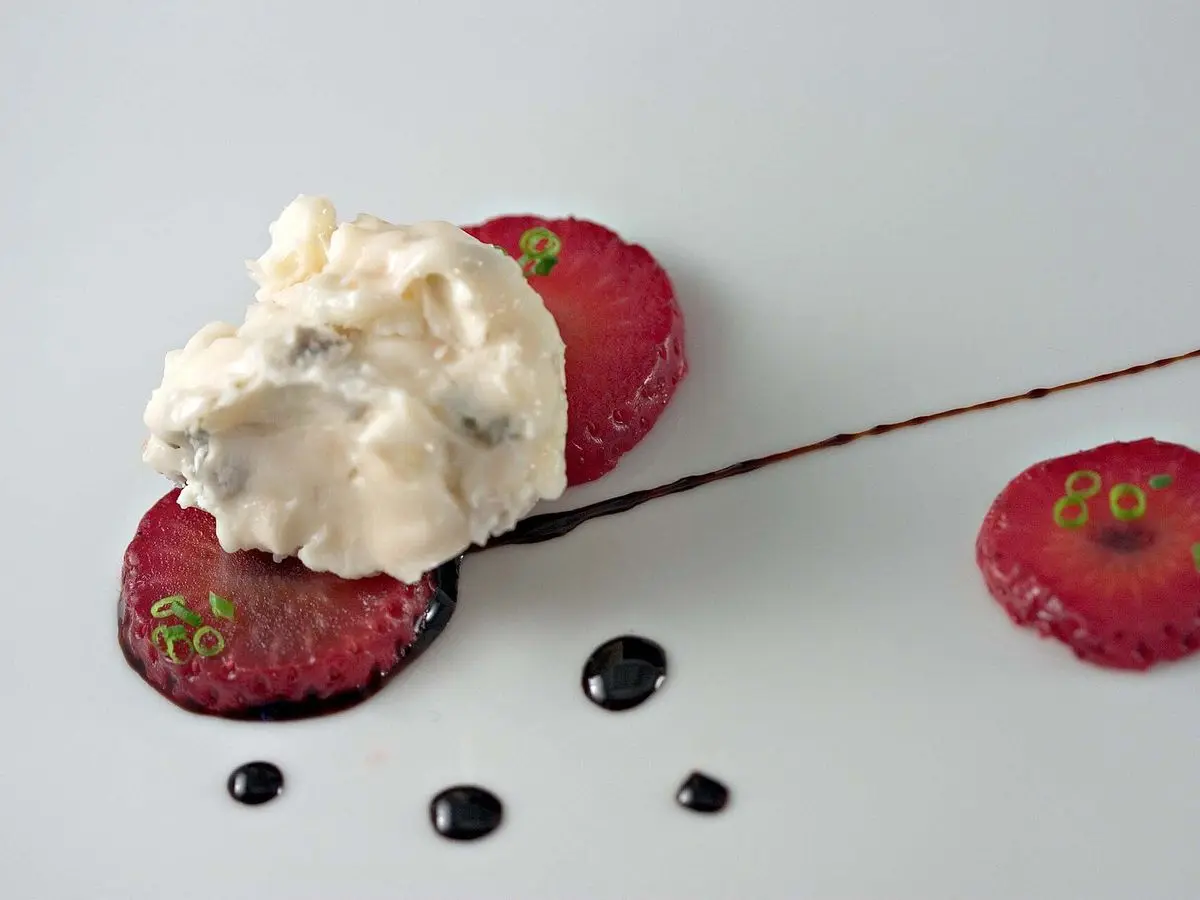 Fresas laminadas con queso cremoso y reducción de vinagre balsámico en un plato blanco