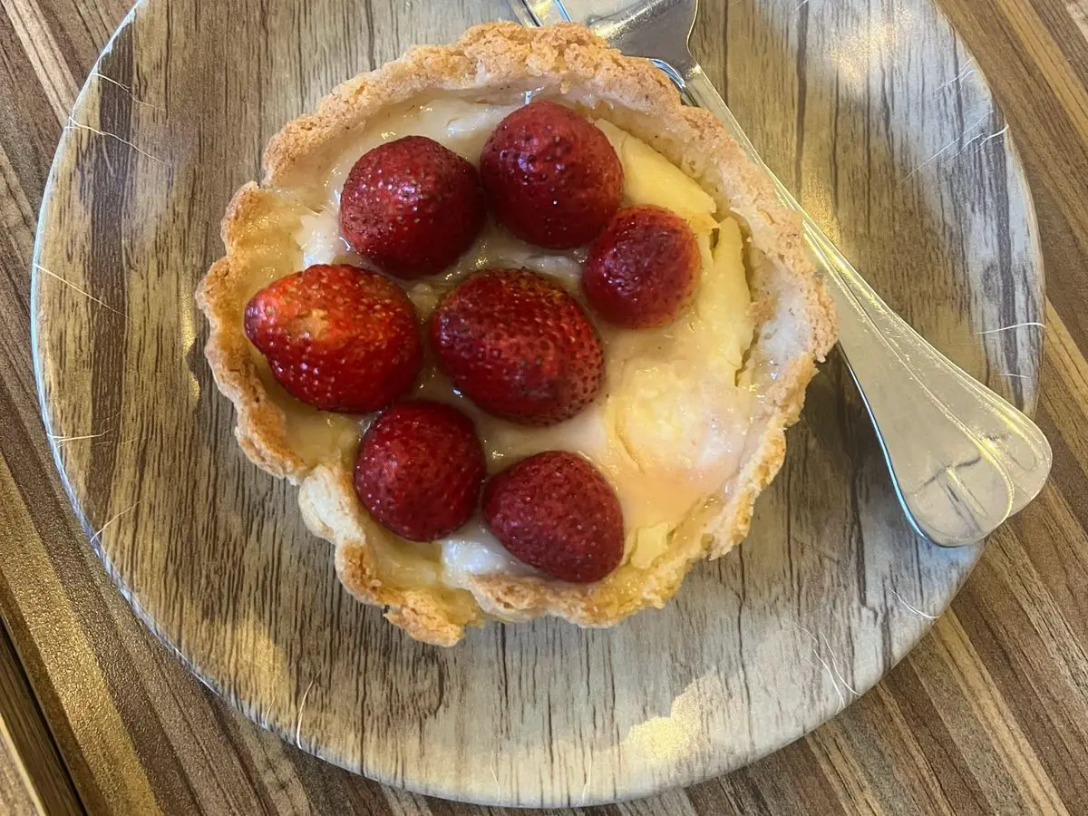 Tartaleta rellena de crema y cubierta de fresas enteras sobre un plato de madera clara