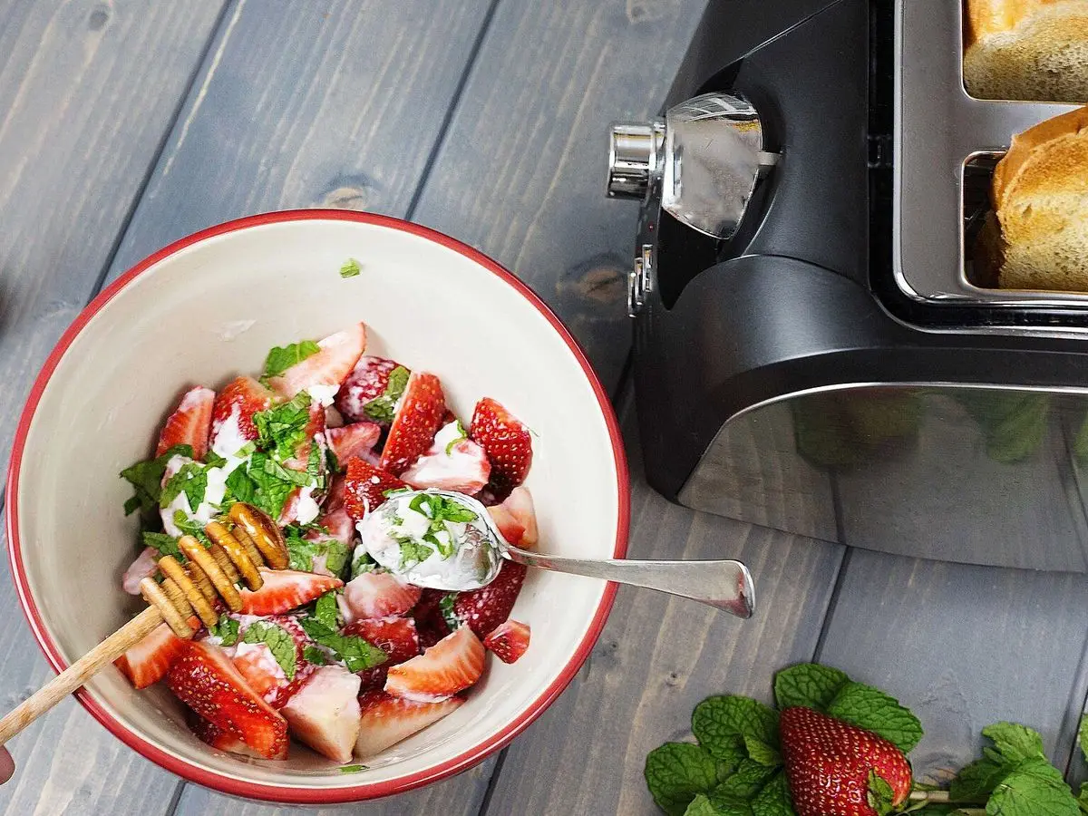 Cuenco con fresas troceadas, hierbabuena y queso fresco, junto a fresas enteras
