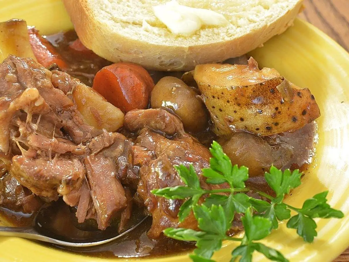 Plato amarillo con guiso de carne en salsa oscura, patata y perejil
