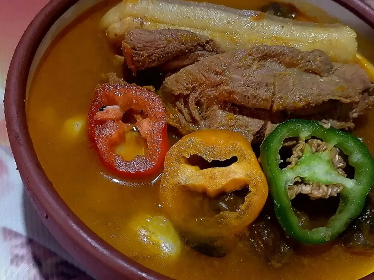 Cuenco de barro con fricasé de cerdo en caldo anaranjado, con maíz y ajíes enteros