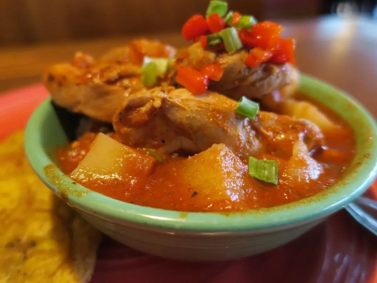 Cuenco de pollo guisado con patatas en salsa de tomate, con pimiento rojo y cebolleta picados por encima