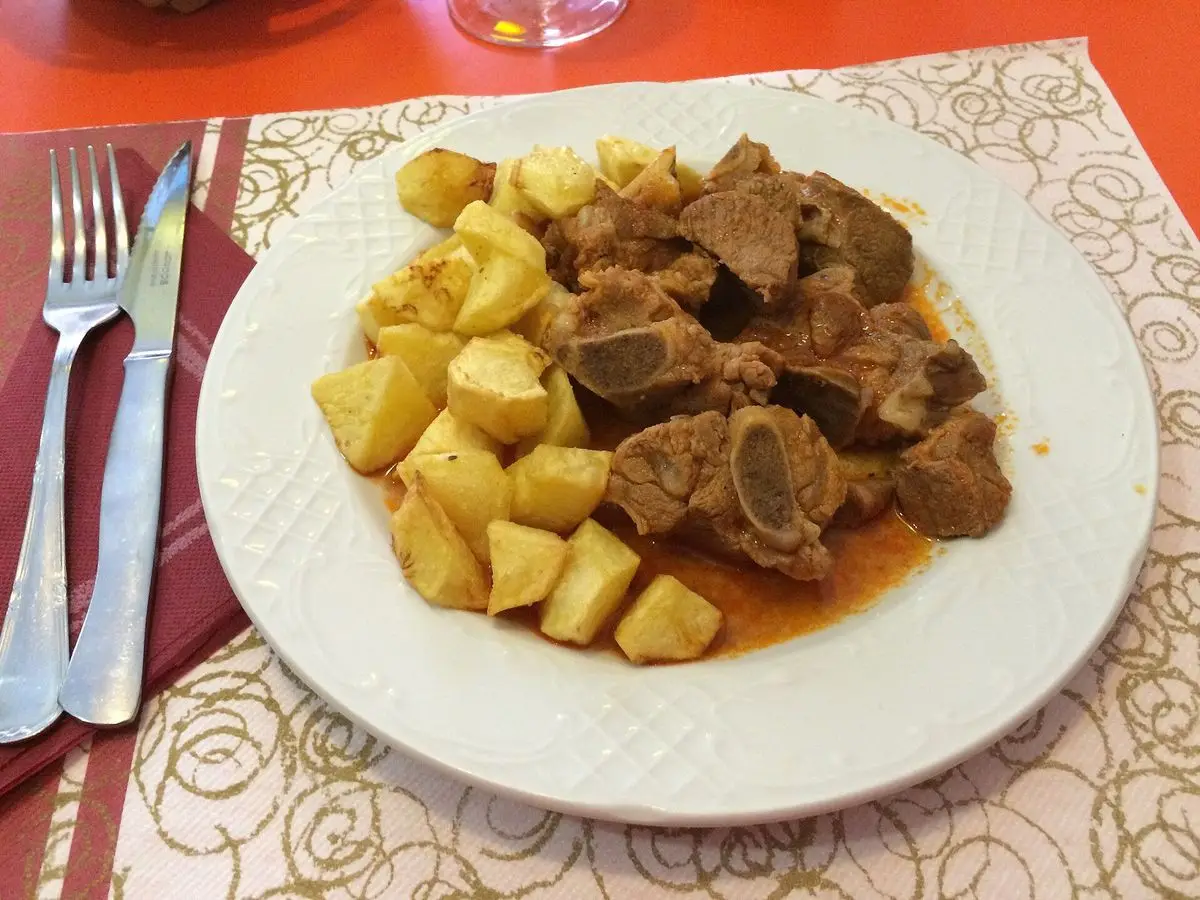 Plato de trozos de cordero en salsa de pimentón con dados de patata