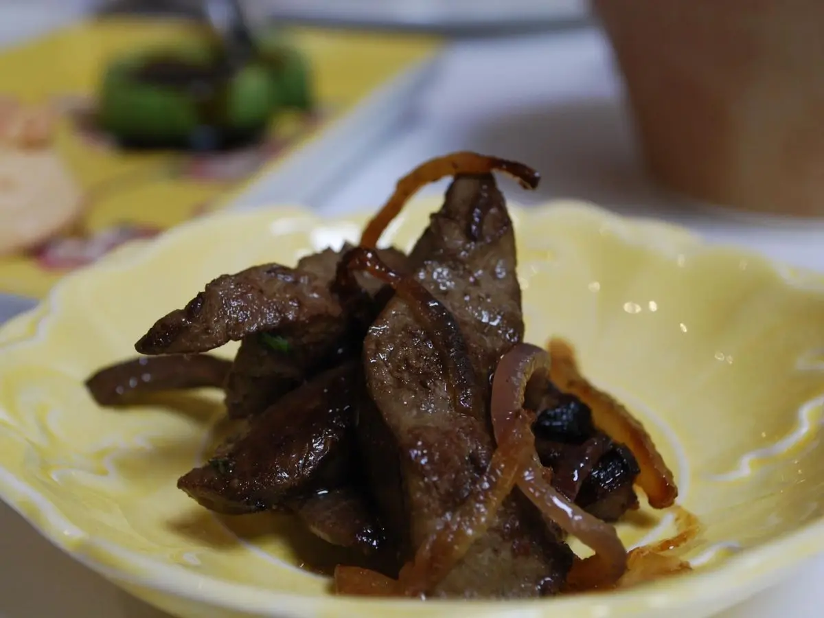 Plato amarillo con trozos de carne y vísceras fritas con cebolla caramelizada