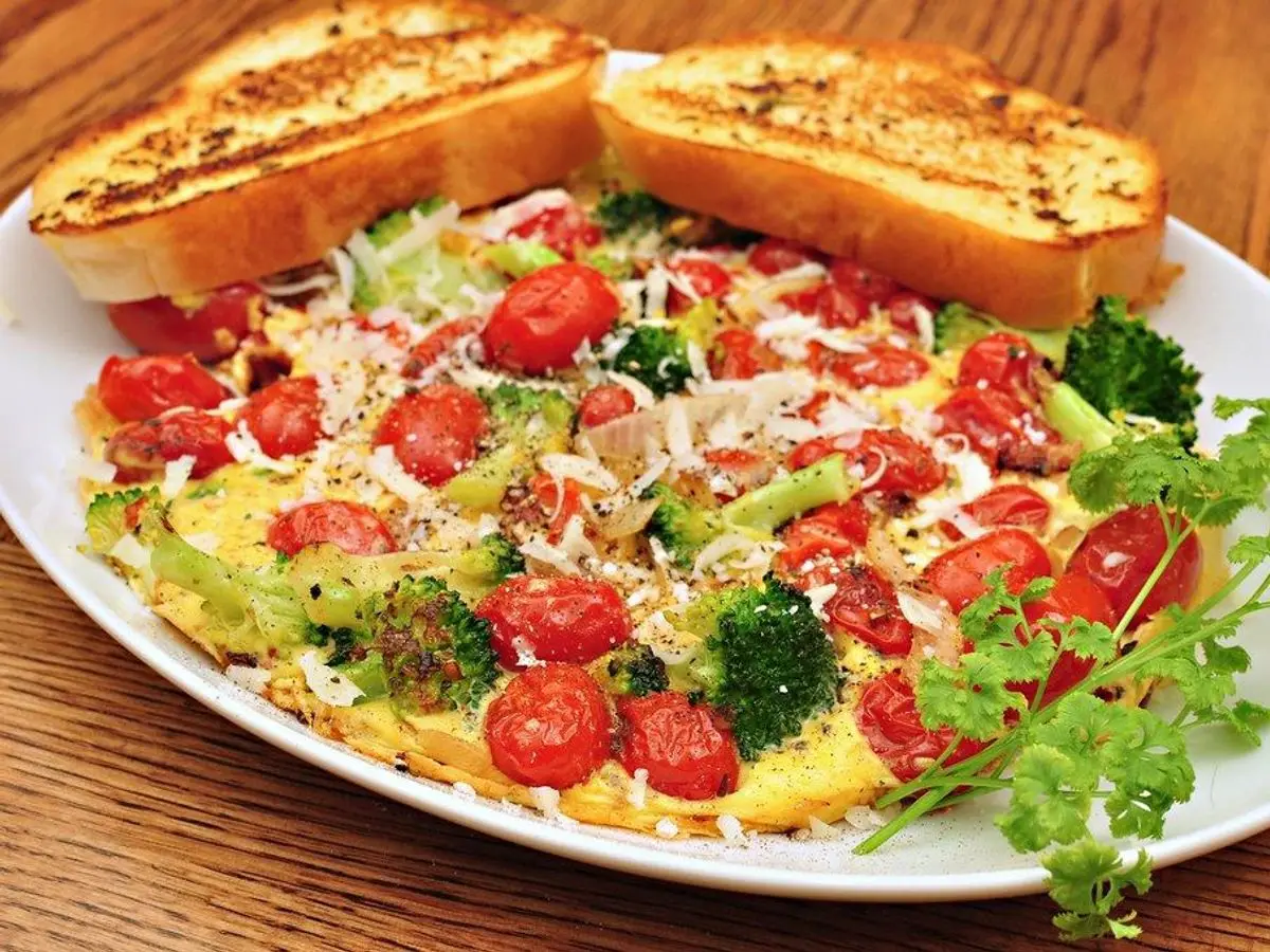 Frittata al horno con brócoli, tomates cherry y perejil, servida con dos tostadas en un plato blanco
