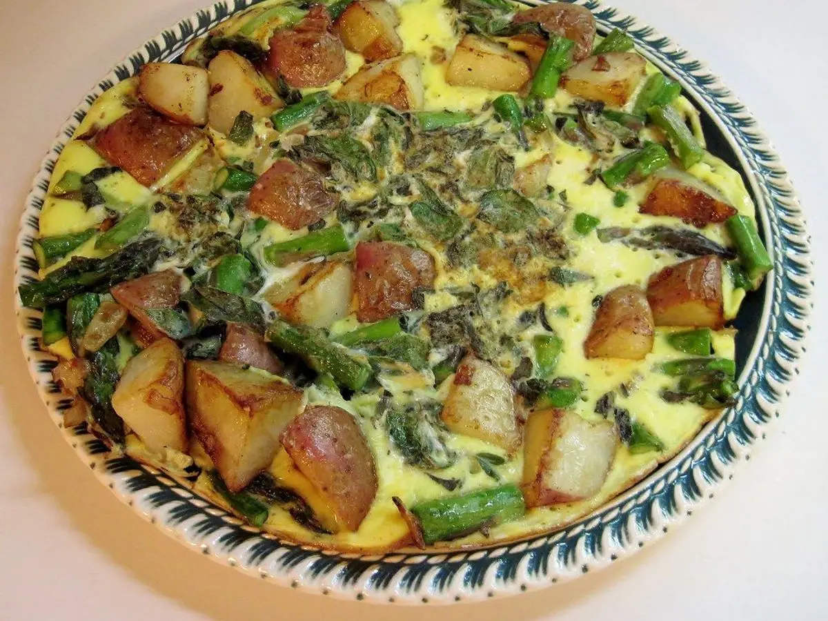Frittata redonda con patatas asadas, espárragos verdes y huevo en un plato con borde azul