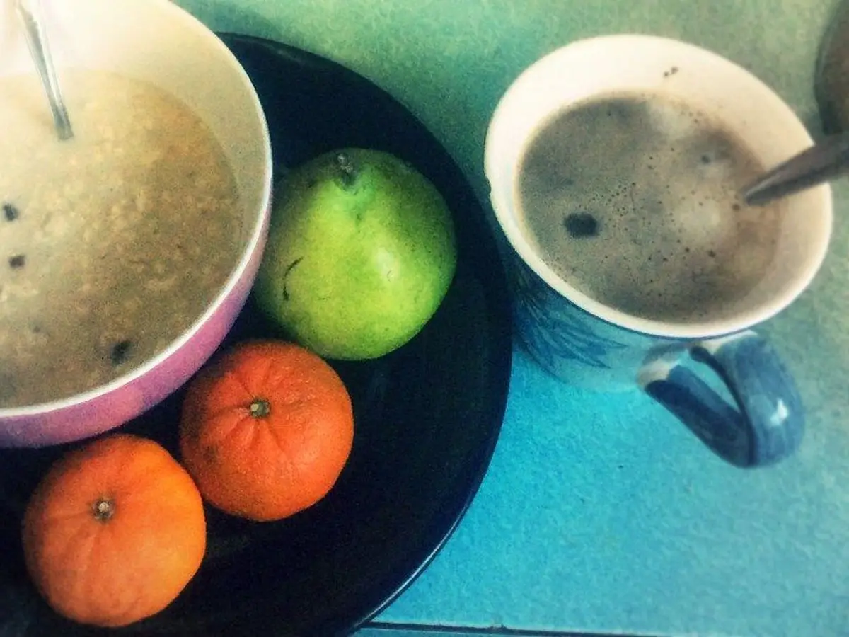 Cuenco de gachas de cereal con una pera verde y mandarinas junto a una taza de café