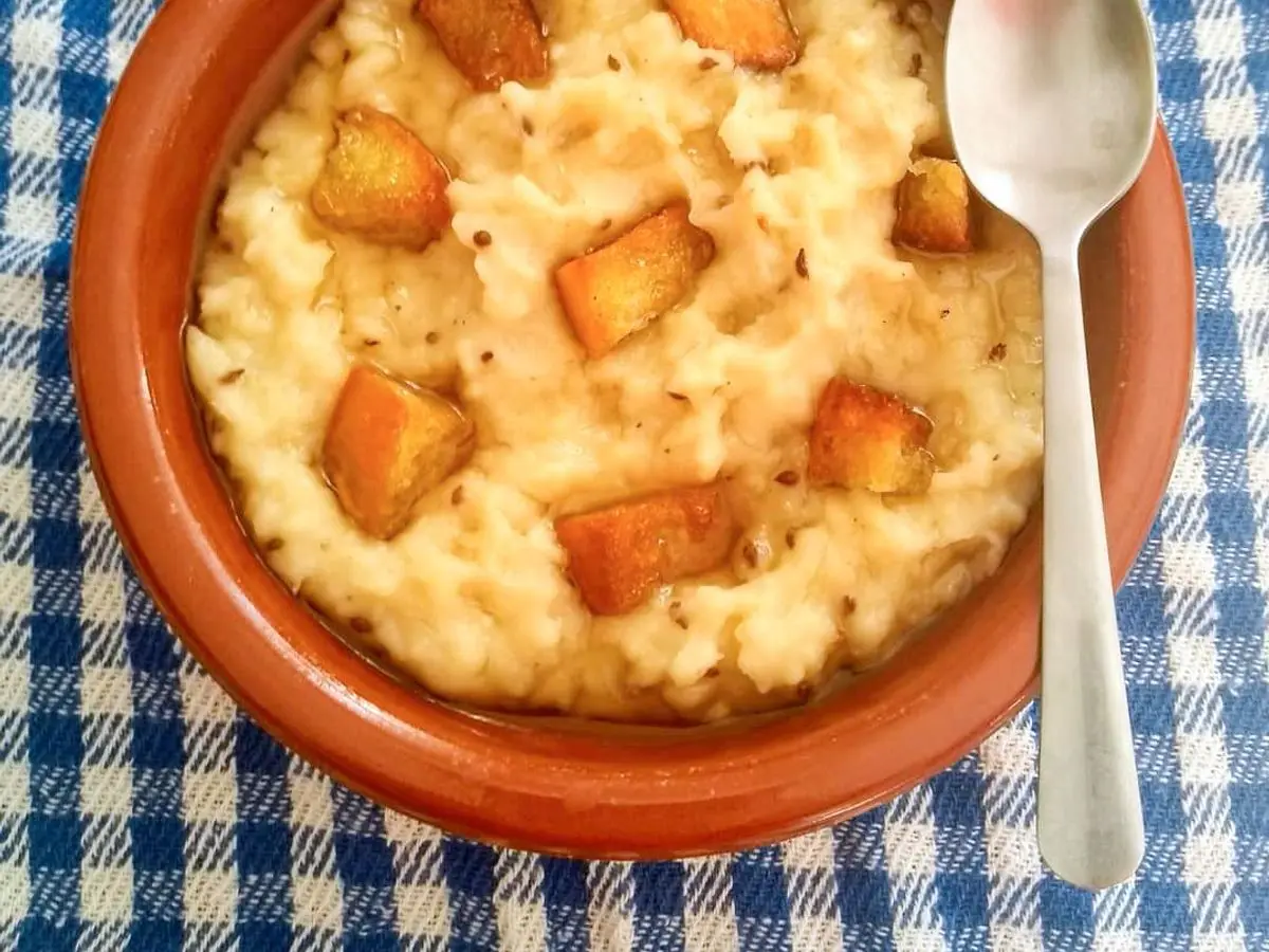Cazuela de barro con gachas dulces cremosas y picatostes de pan dorados, sobre un mantel de cuadros