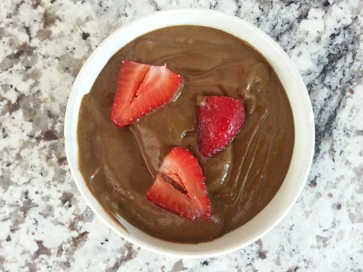 Cuenco blanco con crema espesa de cacao y fresas frescas partidas por encima