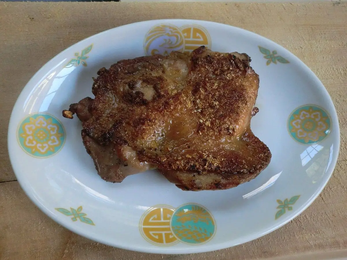 Pollo asado a la parrilla, dorado y jugoso, servido en un plato blanco con decoración verde