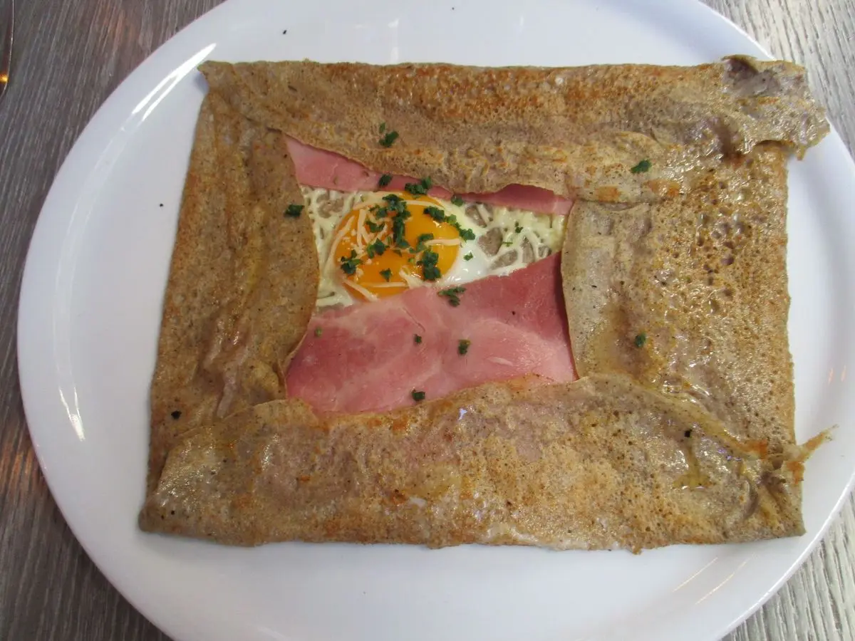 Galette de trigo sarraceno con huevo, jamón y queso en el centro sobre un plato blanco