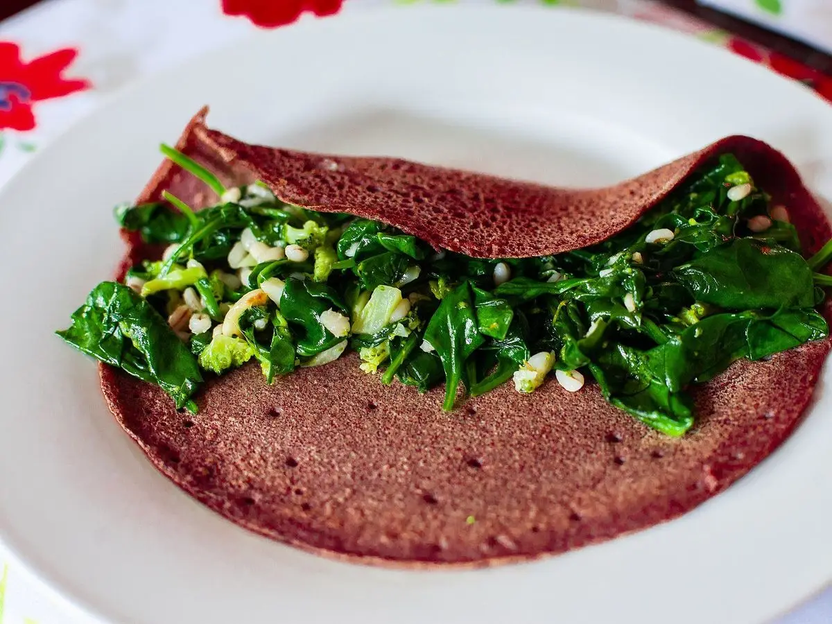 Galette de trigo sarraceno rellena de espinacas salteadas sobre un plato blanco