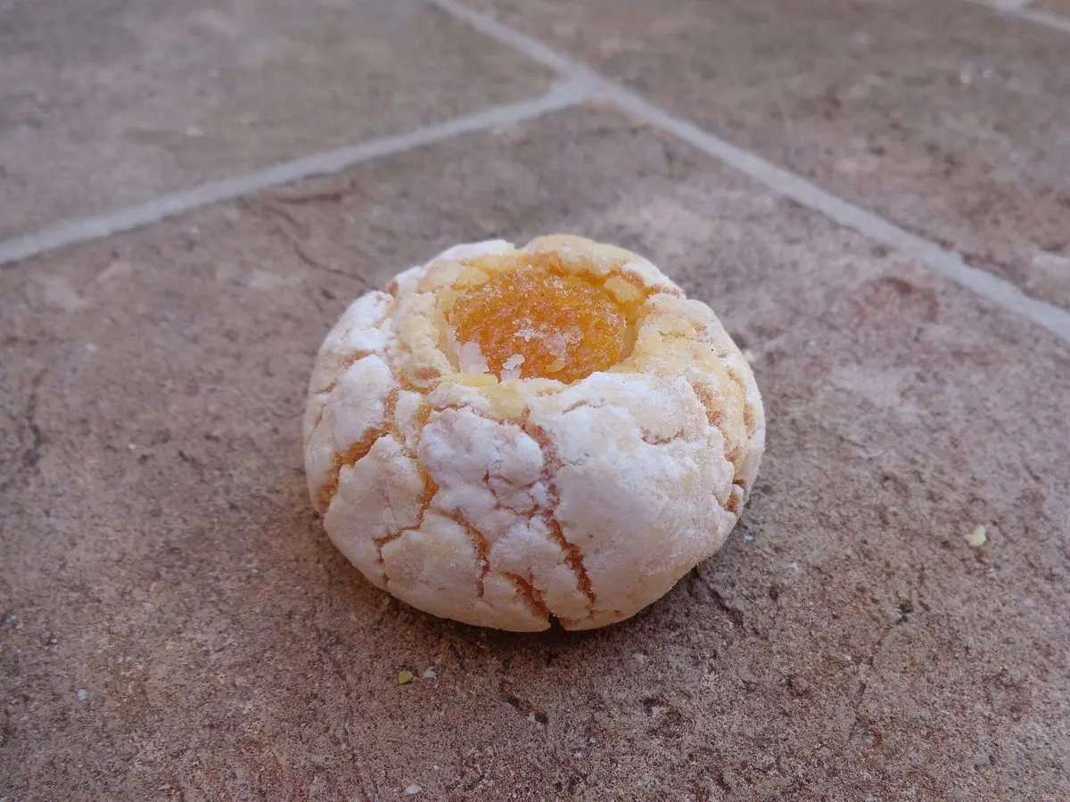 Galleta blanca de almendra con un centro de mermelada anaranjada sobre una superficie de piedra