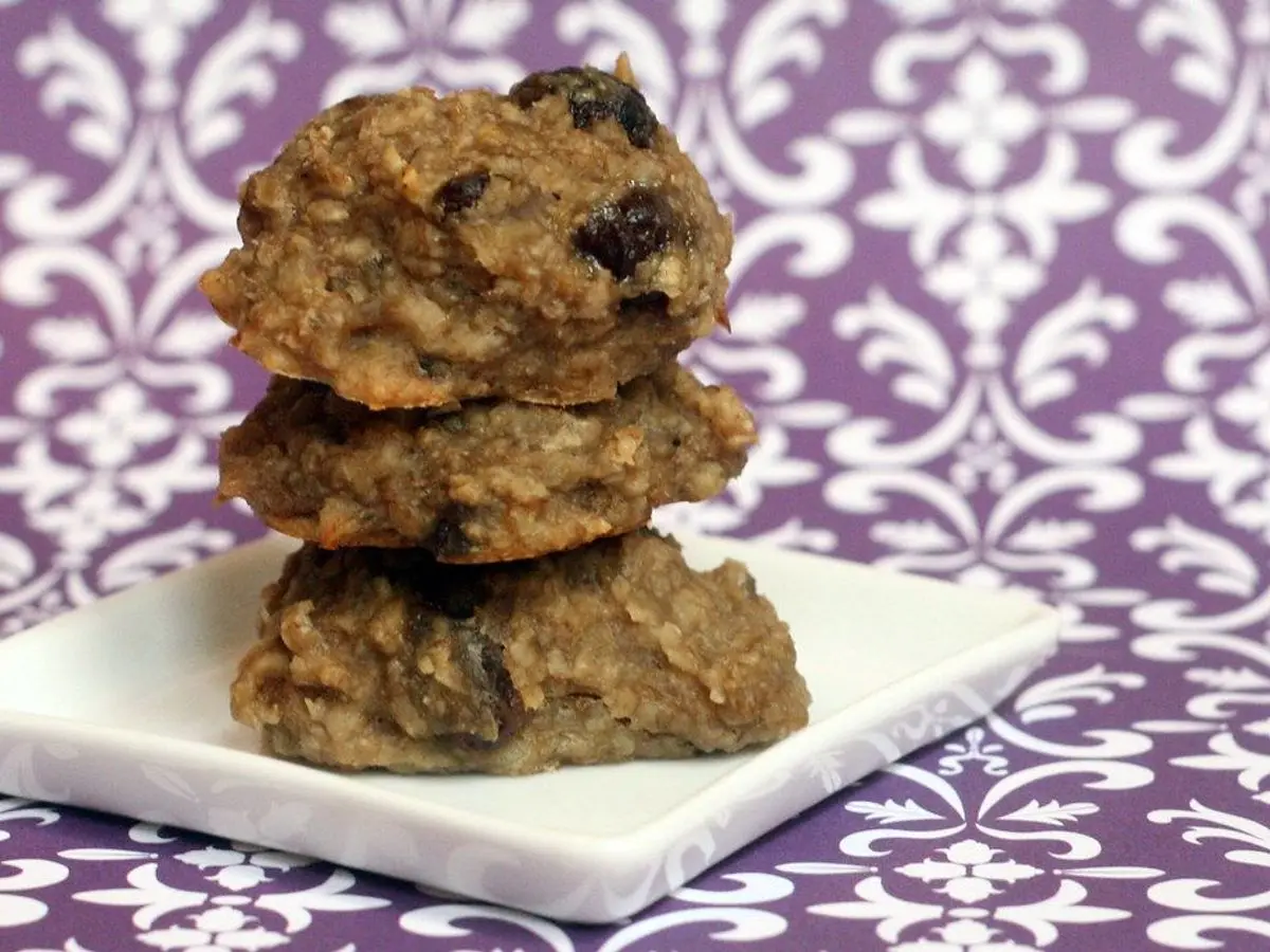 Tres galletas de avena apiladas sobre un plato cuadrado blanco con mantel morado