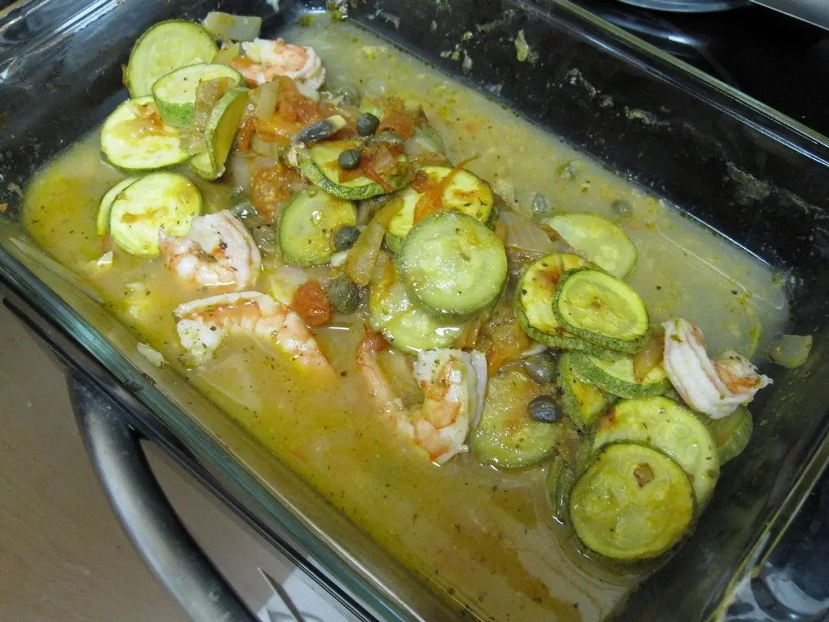 Fuente de cristal con pescado blanco al horno cubierto de rodajas de calabacín y gambas