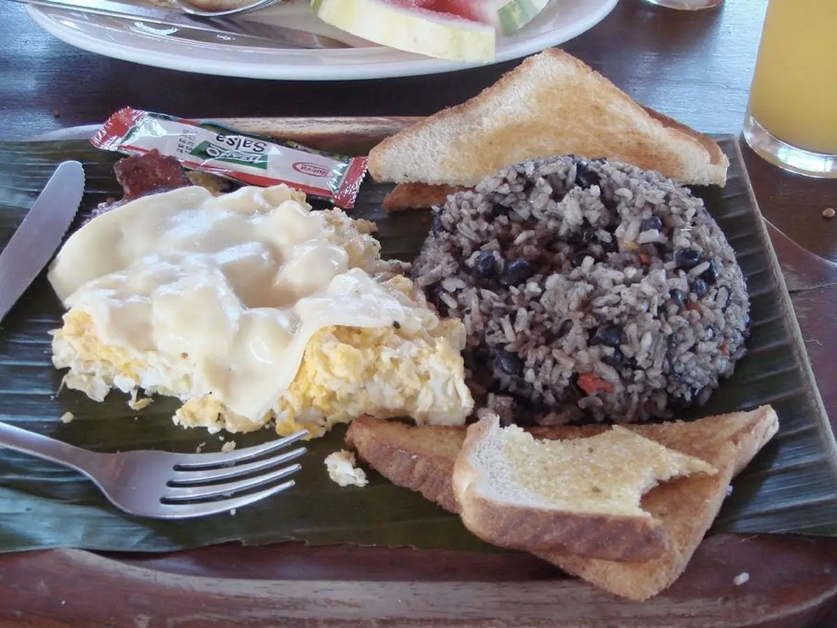 Plato de gallo pinto de arroz y alubias negras con huevo, tortilla y tostada sobre una hoja de plátano