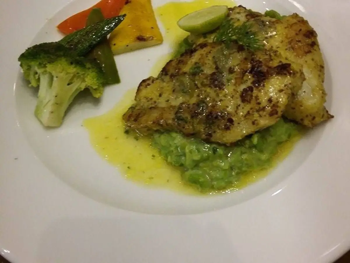 Filete de pescado a la plancha con brócoli, zanahoria, judías verdes y rodaja de lima sobre puré verde en plato blanco