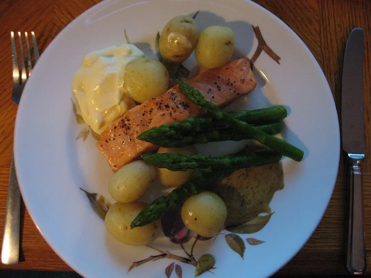 Filete de pescado con salsa holandesa, patatas nuevas cocidas y espárragos verdes en un plato blanco