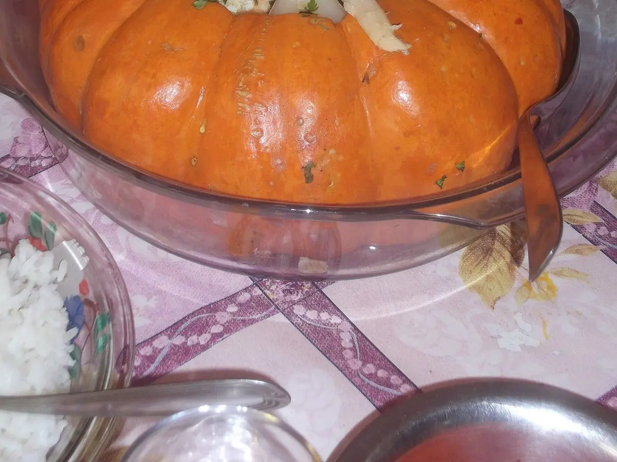 Calabaza asada entera rellena y servida en una fuente de cristal, decorada con palmitos y hierbas