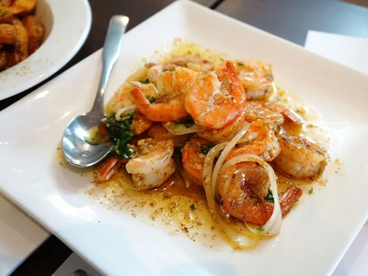 Gambas salteadas con ajo, aros de cebolla y perejil en un plato blanco cuadrado