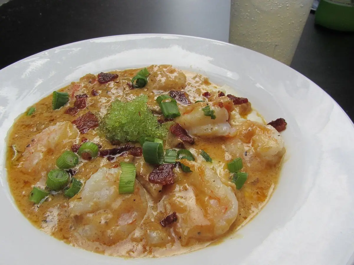 Plato hondo de gambas sobre polenta cremosa con cebolleta picada y salsa dorada