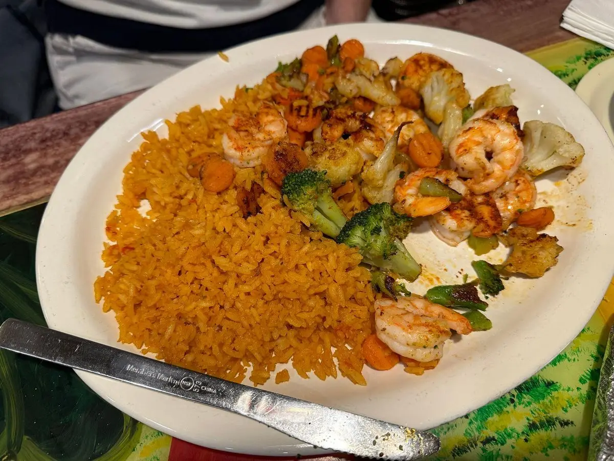 Gambas a la plancha con verduras salteadas y arroz amarillo en un plato blanco