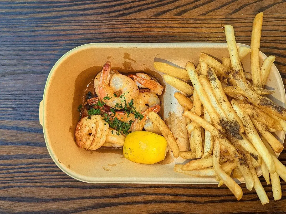 Gambas al ajo con perejil y patatas fritas en tiras, con una rodaja de limón en una bandeja de madera