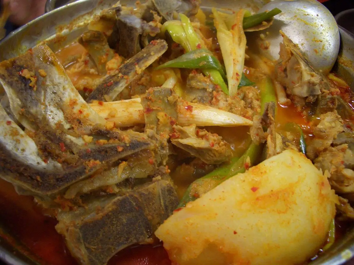 Guiso de huesos de cerdo con patata grande y cebolleta en caldo, servido en cazuela