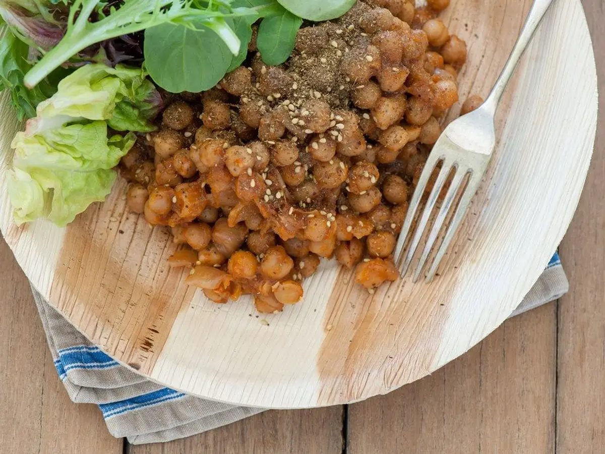 Plato de madera con garbanzos asados especiados y hojas verdes de ensalada, con un tenedor