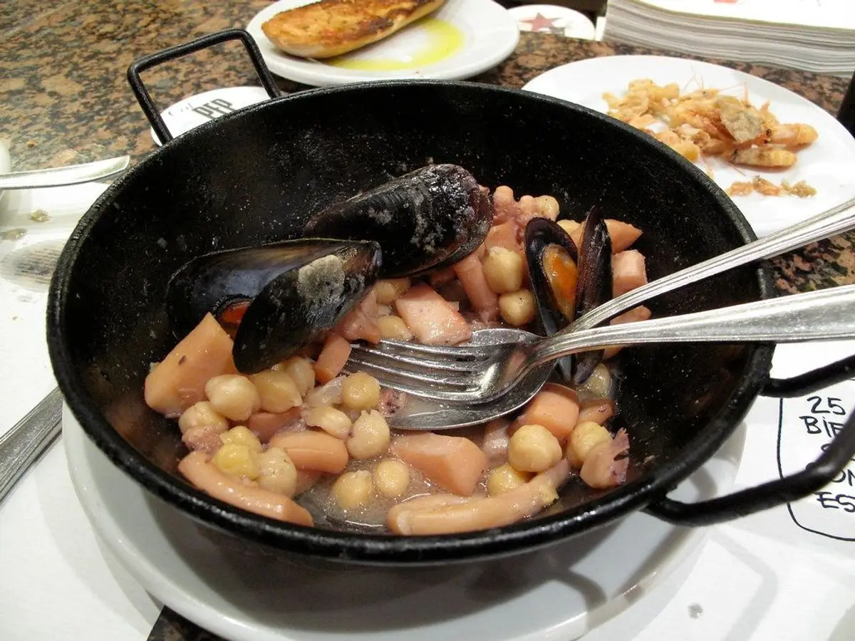 Cazuela negra con garbanzos, zanahoria y mejillones, con tenedores dentro